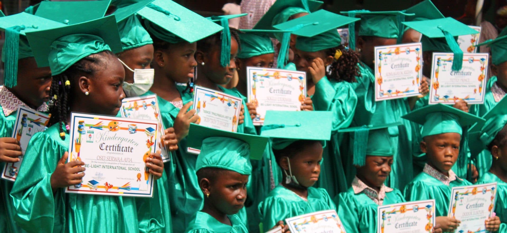 Kindergarten graduates in green gowns holding their certificates at Be-Light International School